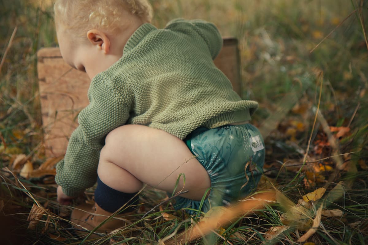 barn med tygblöja i skogsmiljö under hösten. blöjan har ett mönster med rådjur